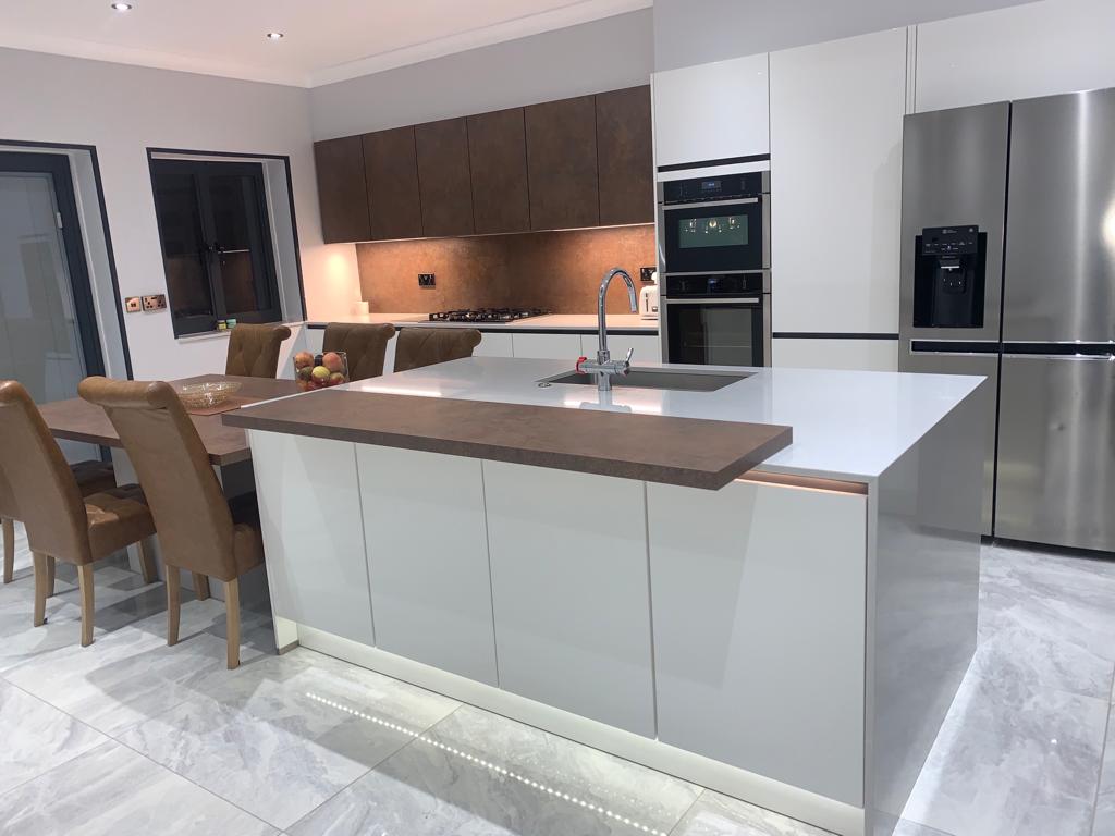 Fitted kitchen with white gloss island and copper splashback